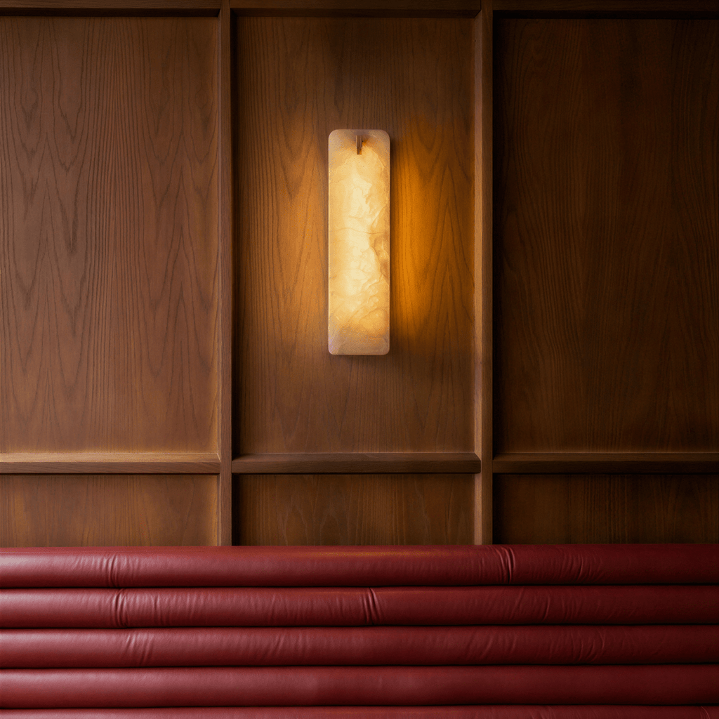 Clérachic marble wall sconce lit against a wood-panelled wall, above a deep red channel-tufted leather banquette.
