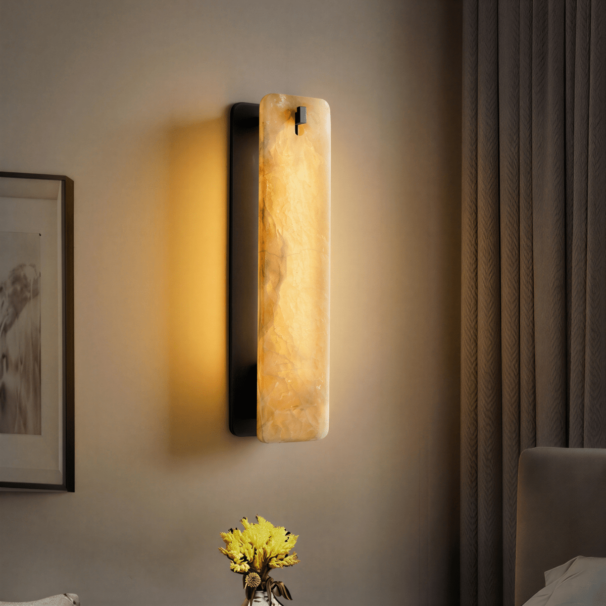 Clérachic marble wall sconce in matte black, lit at a bedside beside a heavy herringbone-woven curtain, with an upholstered headboard and pillow at the lower right.