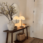 A black Clérachic table lamp lights a rustic console table beside a stoneware vase and woven basket.
