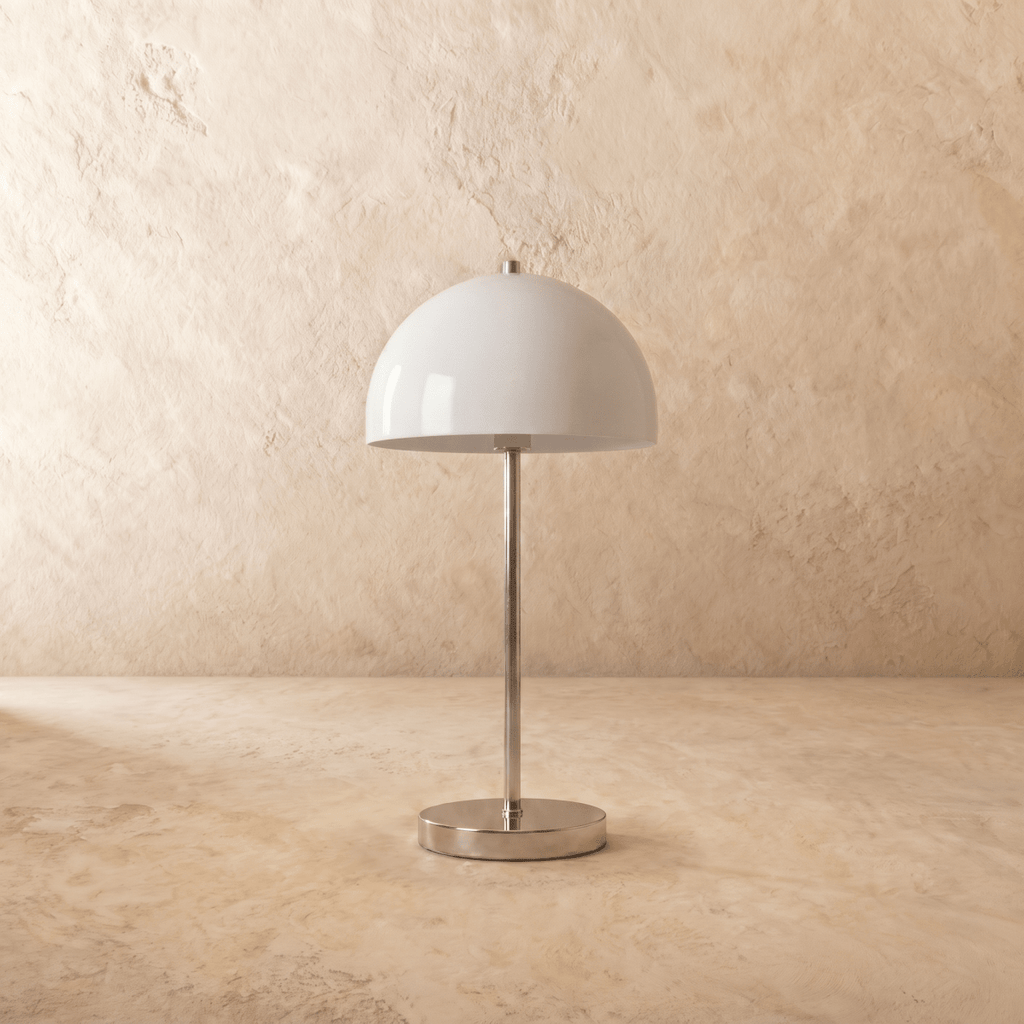 A chrome Clérachic table lamp viewed from a different angle, the white dome shade lit warmly.