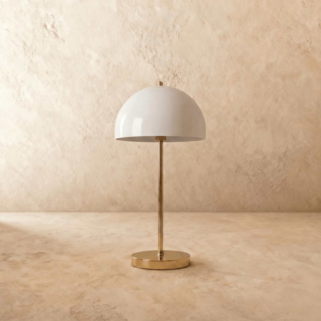 A polished brass Clérachic table lamp viewed from a different angle, the white dome shade lit warmly.