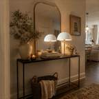This pair of brass Clérachic table lamps lights a console table beneath an arched mirror and framed art.