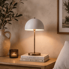 This vintage brass Clérachic table lamp lights a nightstand stacked with books beside a stoneware pitcher.