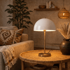 A vintage brass Clérachic table lamp lights a rattan coffee table beside a pampas grass arrangement.