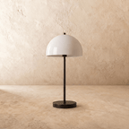 This black Clérachic table lamp is shown from another angle, its white dome shade glowing softly.