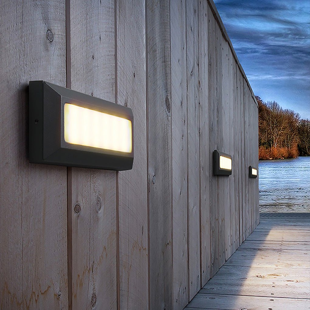 Three of the lights lit along a timber-clad wall beside water, autumn woodland behind.