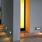 The step lights low on grey rendered walls, lighting a passage beside a glowing amber doorway.