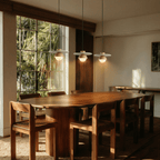 Clérachic pendant lights in light wood hanging above a sunlit dining table with woven wood chairs.