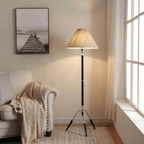 Clérachic tripod floor lamp in black and chrome, lit in a corner beside a nailhead-trimmed sofa, its cord running away across the floor.