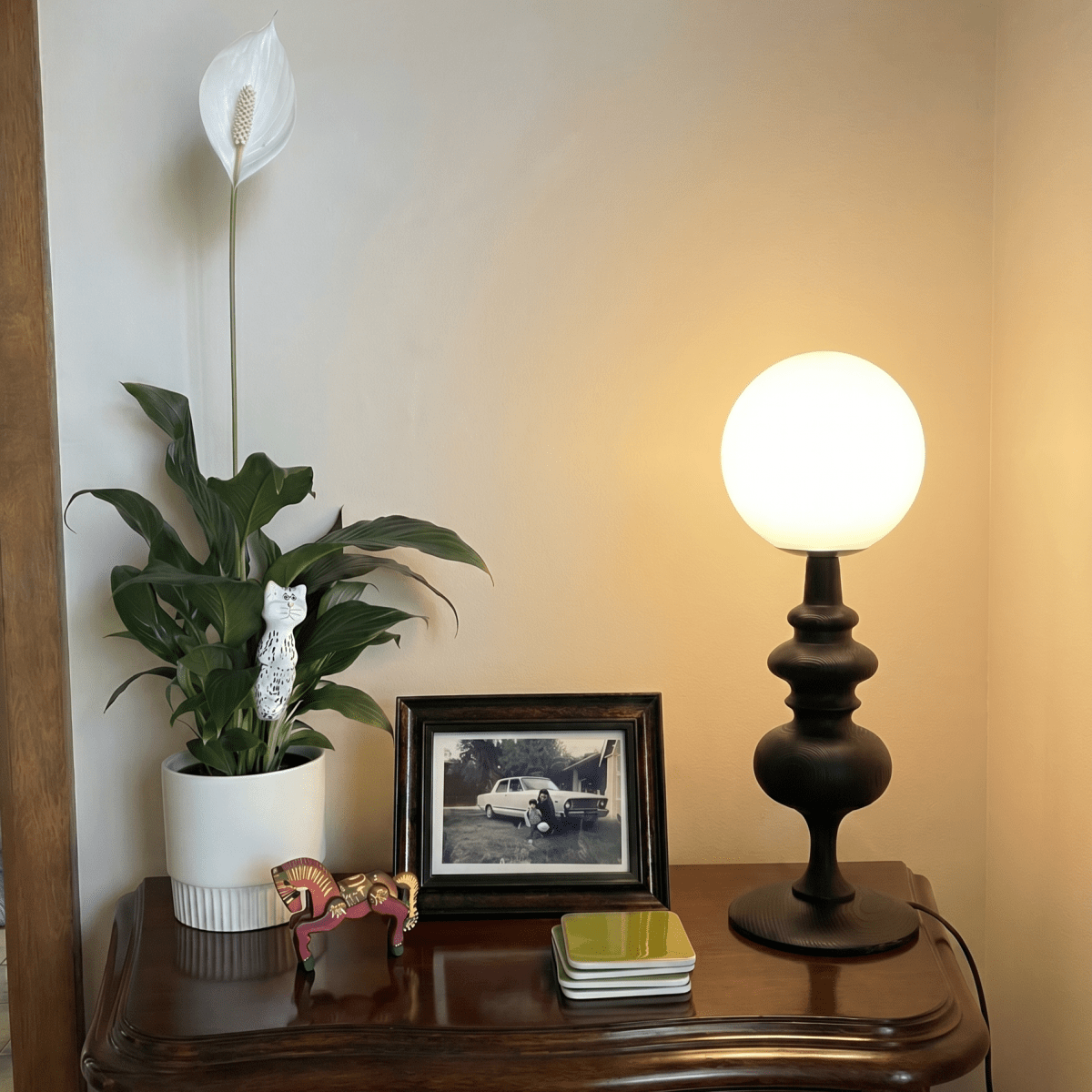 Clérachic table lamp in matte black glowing on a dark wood dresser beneath a framed vintage photograph.