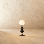 Clérachic table lamp in matte black glowing warm, a turned base beneath a round opal glass globe.