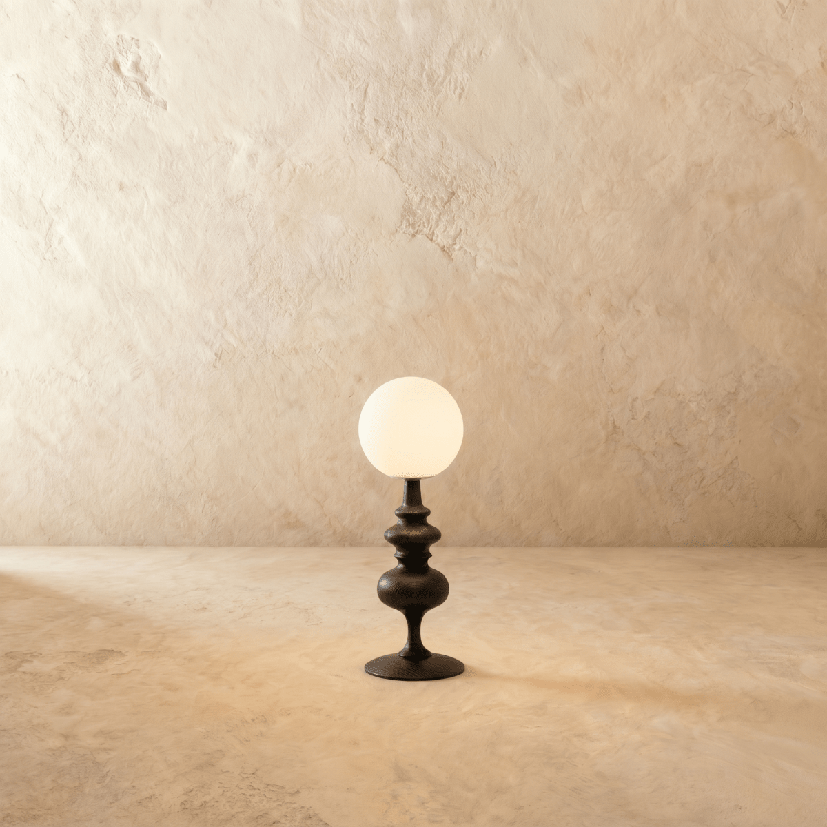 Clérachic table lamp in matte black glowing warm, a turned base beneath a round opal glass globe.
