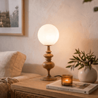 Clérachic table lamp in walnut glowing on a side table beside a stack of books and a small vase.