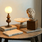 Clérachic table lamp in walnut glowing on a round table beside stacked books and a small sculpture.