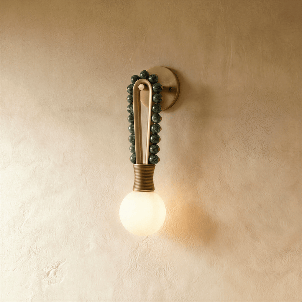 Clérachic wall light in green marble, its stone spheres arching over the metal hairpin and running down the far side, lit on the same limewash backdrop.