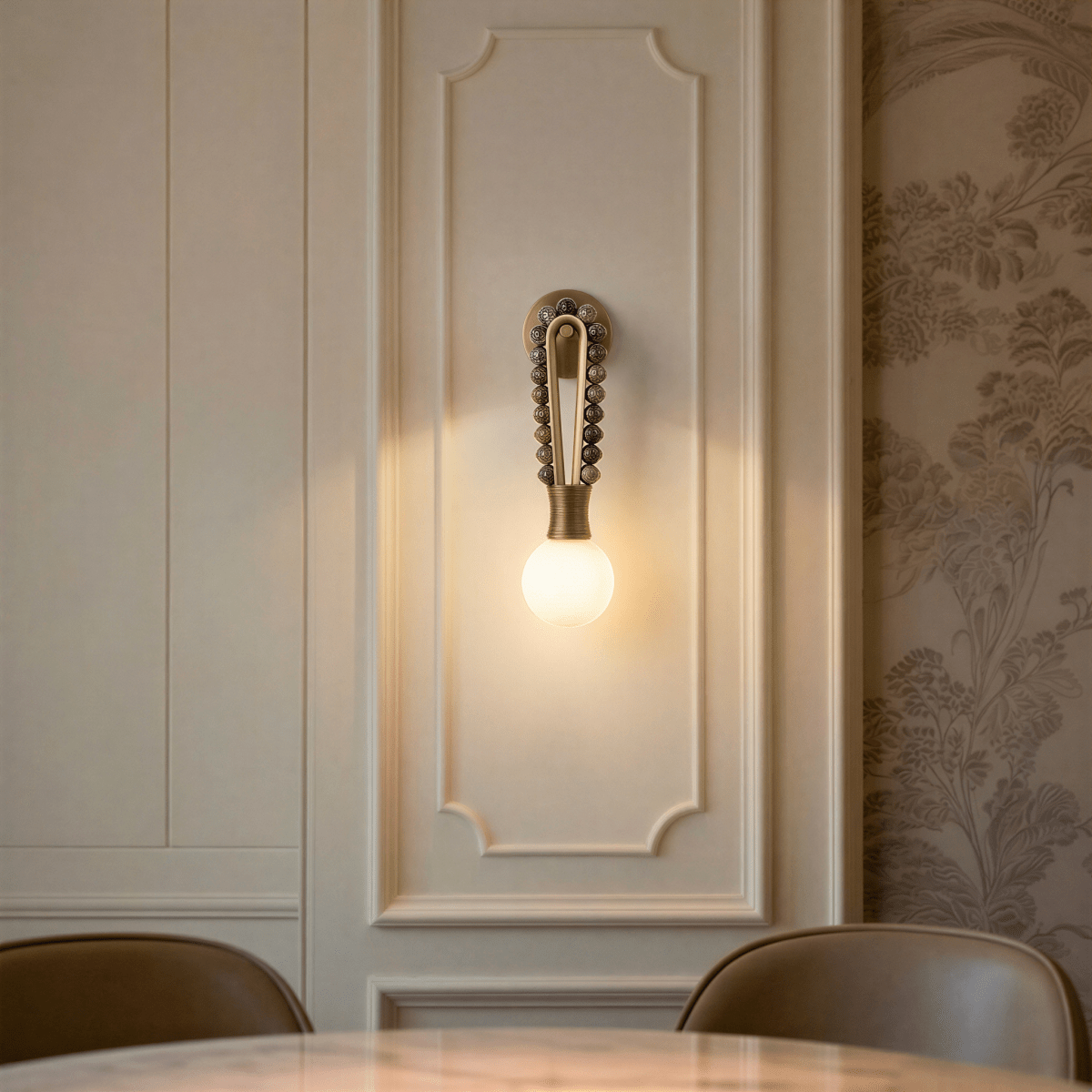 Clérachic wall light in brown marble, lit on an ornate panelled wall beside floral wallpaper, above a round table with a veined marble top and leather chairs.