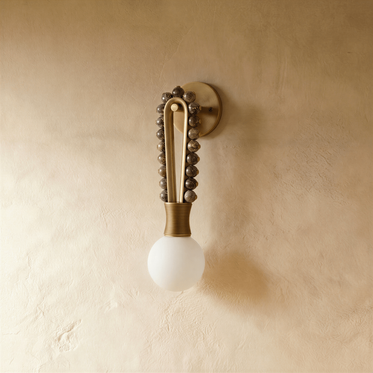 Clérachic wall light in brown marble shown with the globe dark, so the flecked stone and the ribbed collar read clearly against bare plaster.