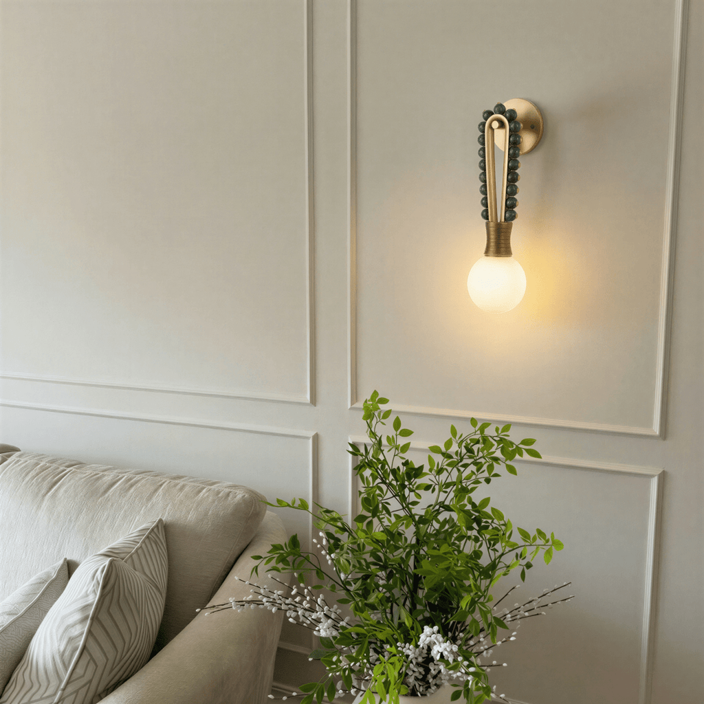Clérachic wall light in green marble, mounted on a panelled living-room wall beside a sofa with cushions and a flowering plant.
