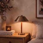 Clérachic table lamp in vintage brass on a nightstand with stacked books and a jug of dried branches.