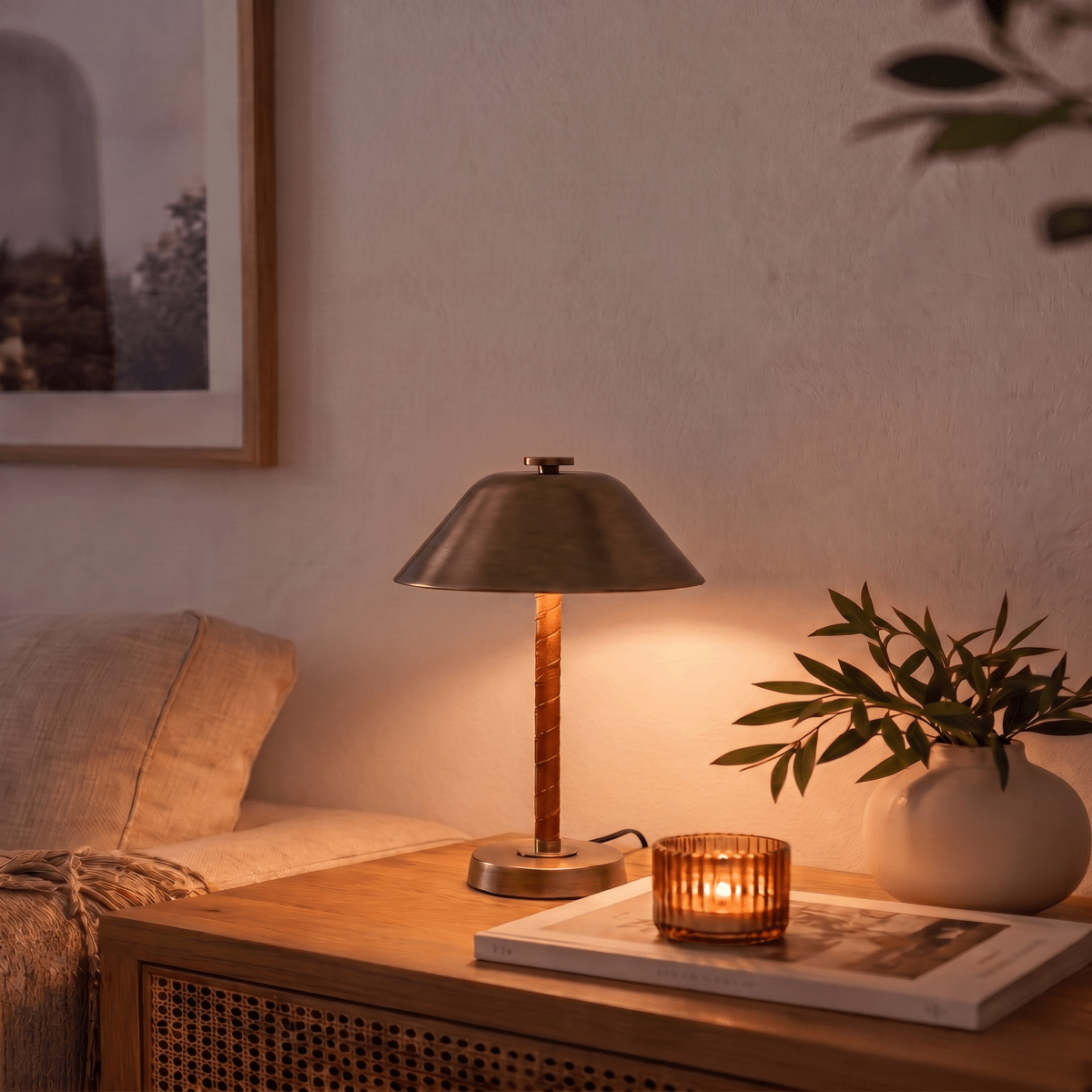 Clérachic table lamp in vintage brass on a side table beside a lit candle and a leafy vase.