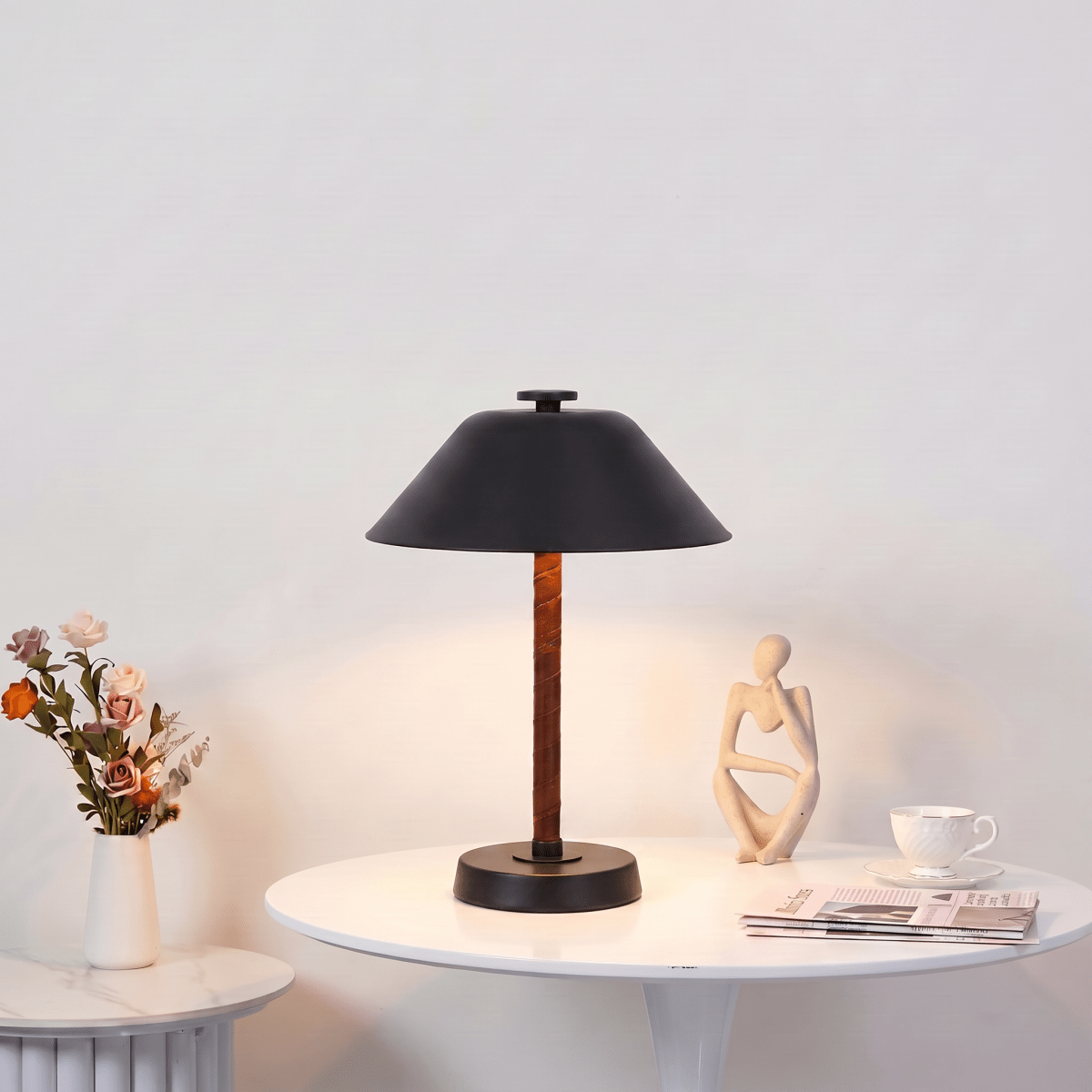 Clérachic table lamp in matte black on a round side table with fresh flowers and a small sculpture.