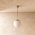 Clérachic globe pendant light in polished brass, shown from a slightly closer studio angle against a plaster wall.