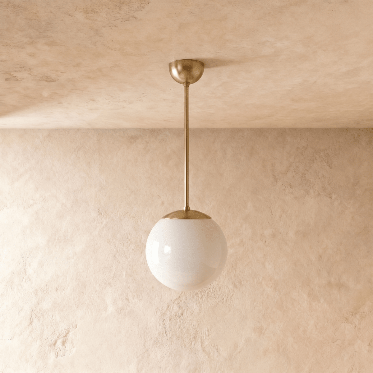 Clérachic globe pendant light in polished brass, shown from a slightly closer studio angle against a plaster wall.