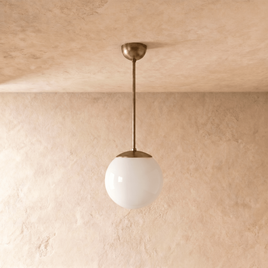 Clérachic globe pendant light in vintage brass, shown from a slightly closer studio angle against a plaster wall.