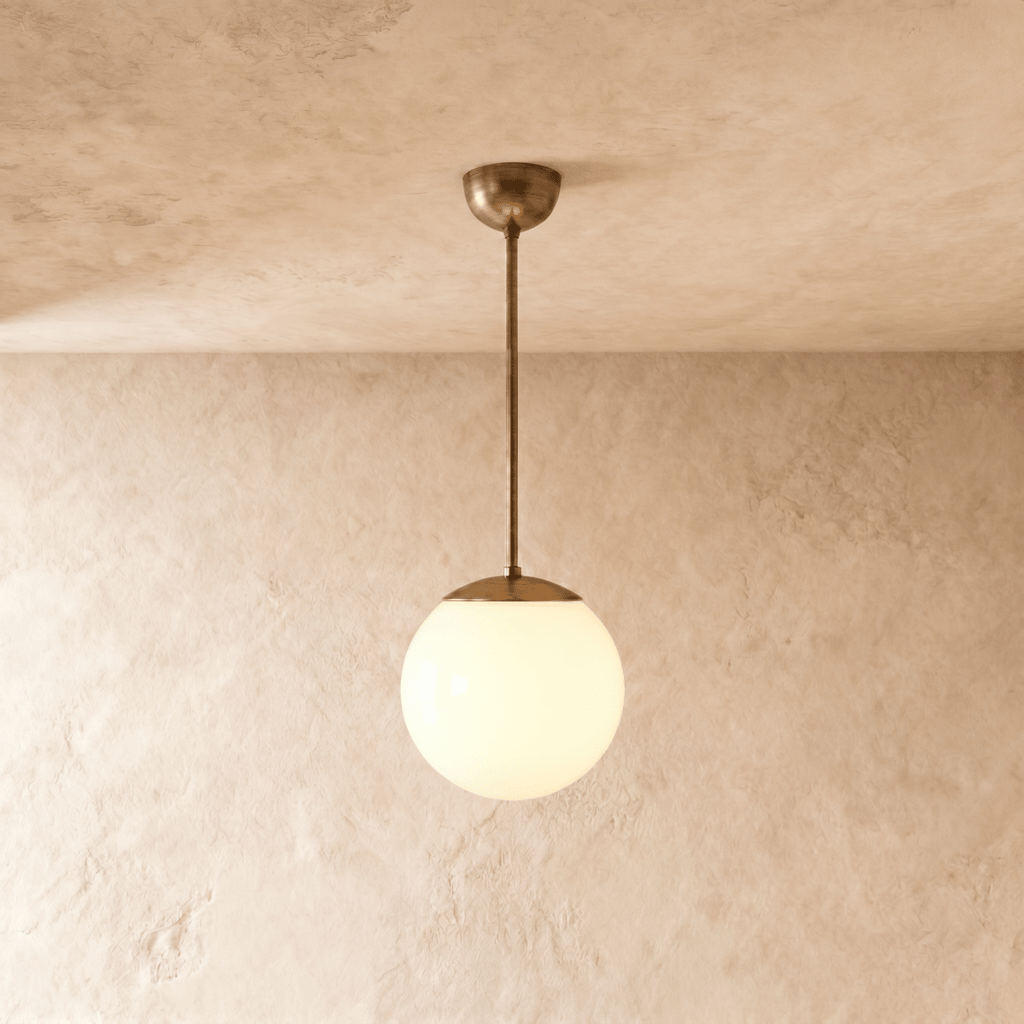 Clérachic globe pendant light in vintage brass, hung on a rod from a plaster ceiling and photographed in studio.