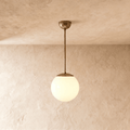 Clérachic globe pendant light in vintage brass, hung on a rod from a plaster ceiling and photographed in studio.