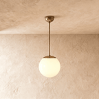 Clérachic globe pendant light in vintage brass, hung on a rod from a plaster ceiling and photographed in studio.