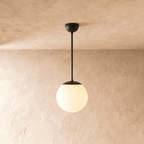 Clérachic globe pendant light in matte black, hung on a rod from a plaster ceiling and photographed in studio.