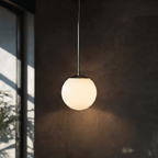 Clérachic chrome globe pendant light lit against a dark wall beside a glass door and a leafy plant.