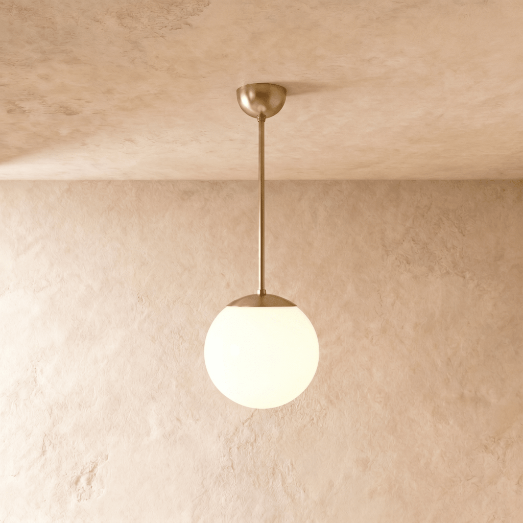 Clérachic globe pendant light in polished brass, hung on a rod from a plaster ceiling and photographed in studio.