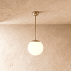 Clérachic globe pendant light in polished brass, hung on a rod from a plaster ceiling and photographed in studio.