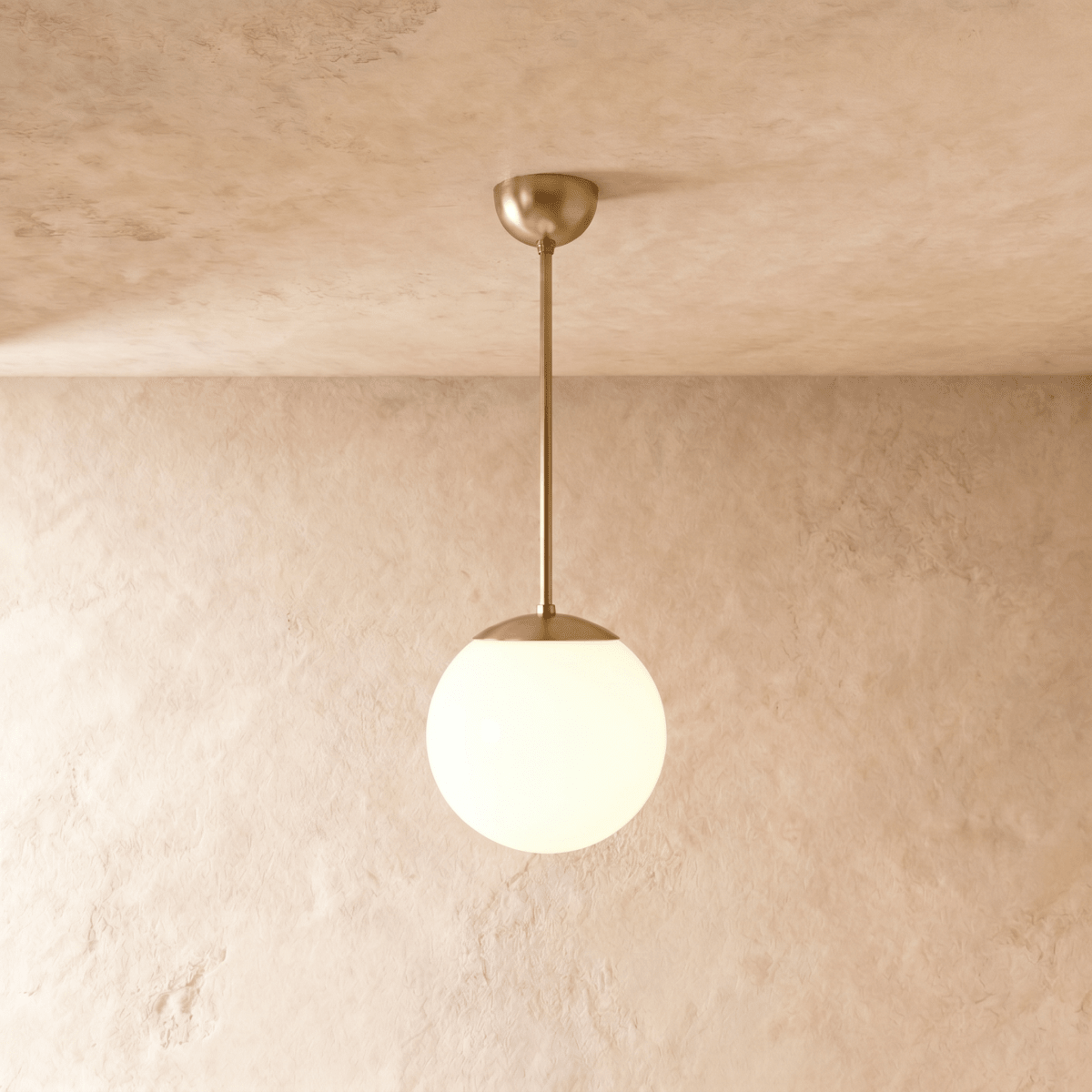 Clérachic globe pendant light in polished brass, hung on a rod from a plaster ceiling and photographed in studio.