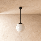 Clérachic globe pendant light in matte black, shown from a slightly closer studio angle against a plaster wall.