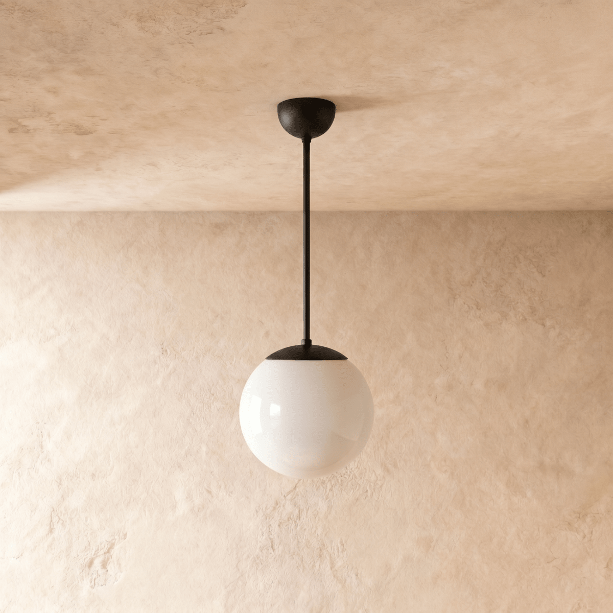 Clérachic globe pendant light in matte black, shown from a slightly closer studio angle against a plaster wall.
