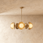 Clérachic chandelier in a brighter brass finish, its row of overlapping discs and opal globes below a ceiling.