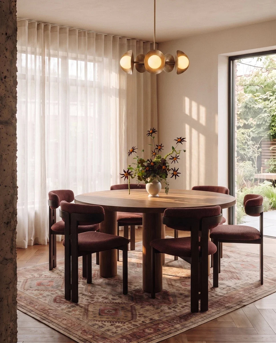 Clérachic vintage brass chandelier glowing above a round table with maroon chairs beside glass garden doors.