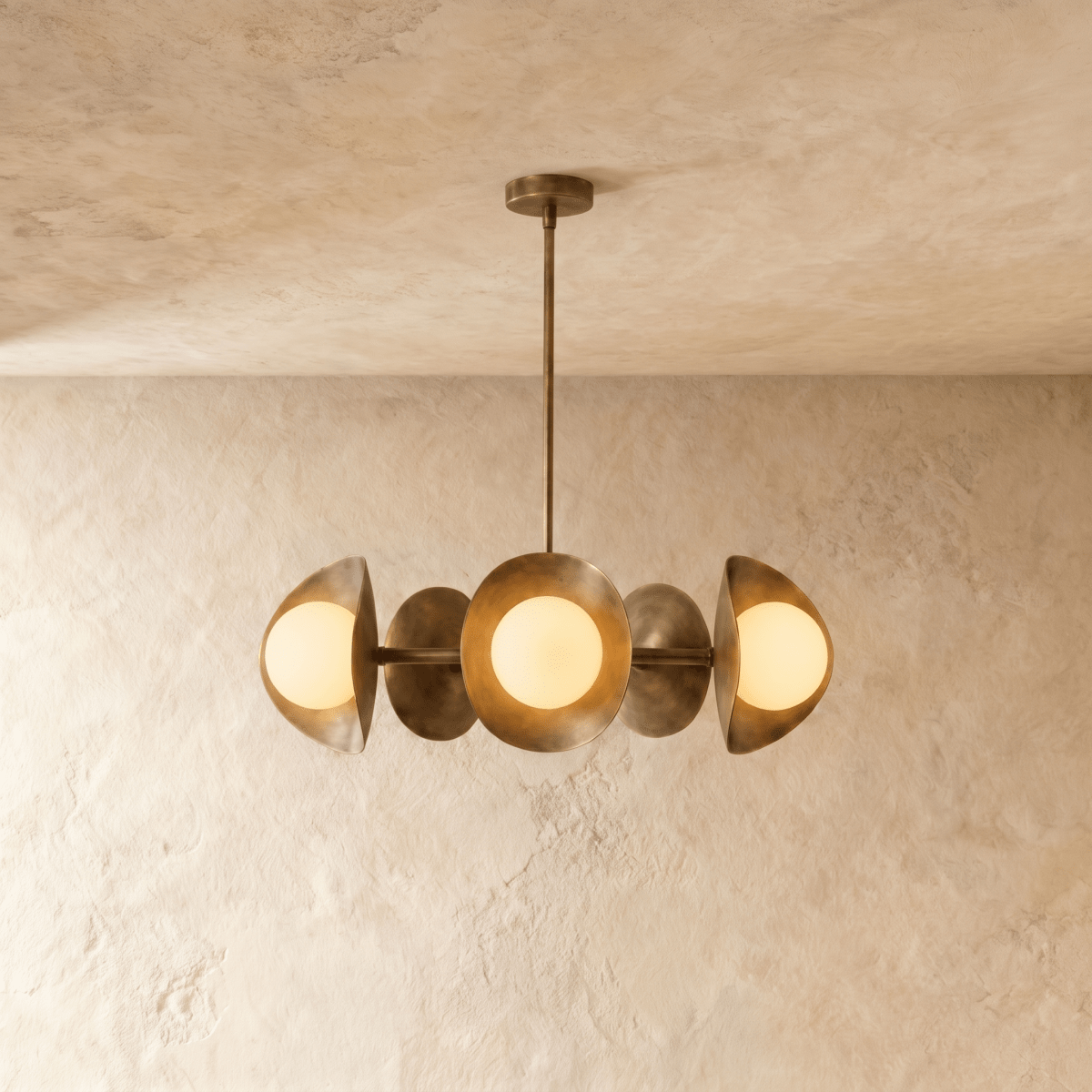 Clérachic chandelier in vintage brass, its row of overlapping discs and opal glass globes below a plaster ceiling.