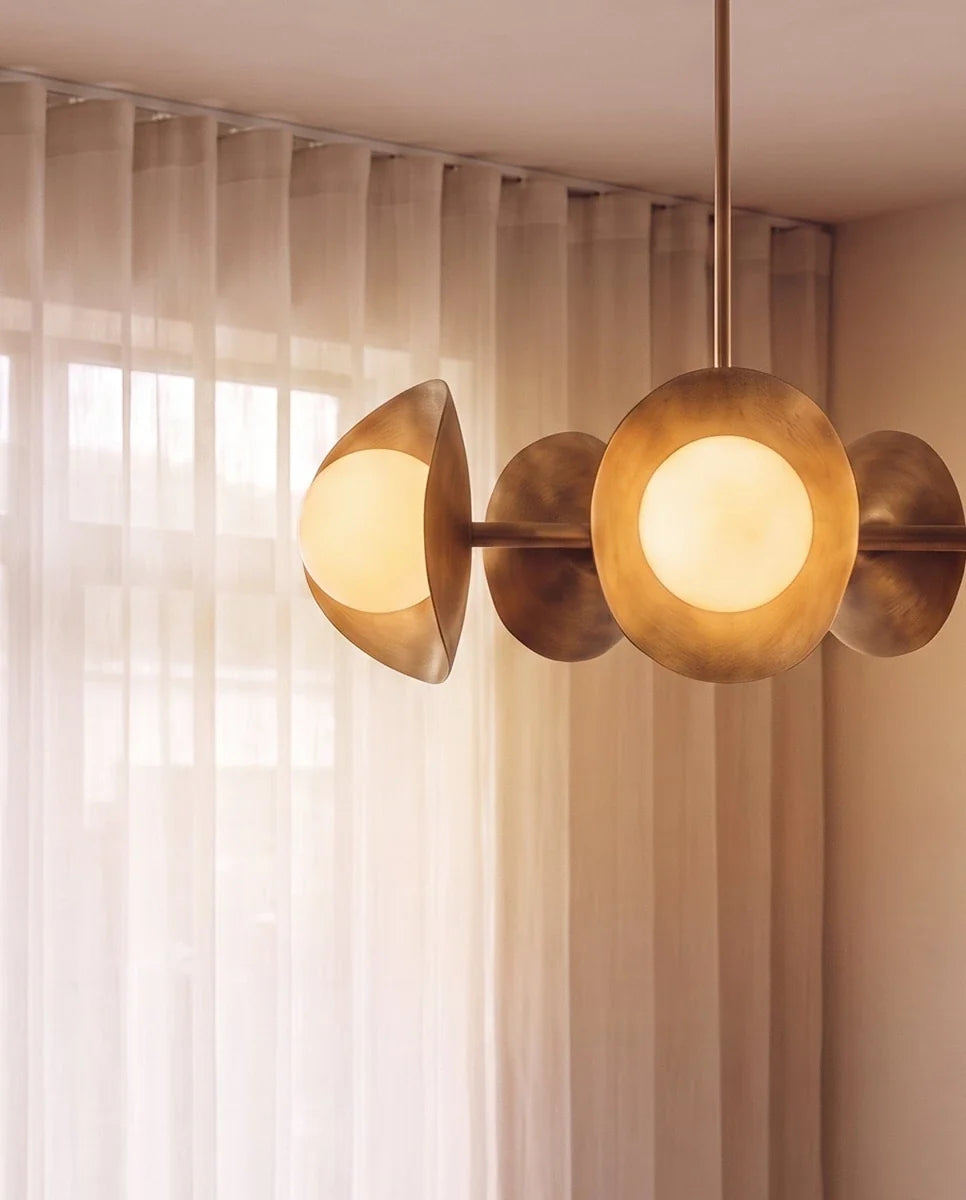 Clérachic vintage brass chandelier, its disc shades and glass globes glowing in close-up beside sheer curtains.