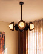 Clérachic matte black chandelier glowing beside sheer curtains and a framed painting in a sunlit corner room.
