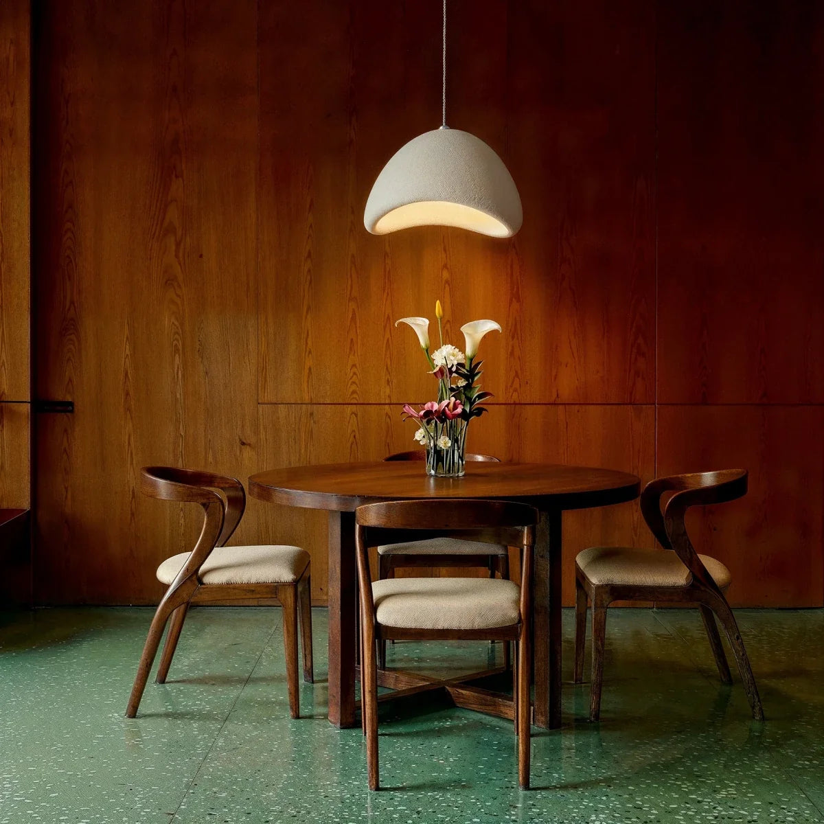 Clérachic Shibui pendant light above a round wooden dining table set with calla lilies, its pale shade standing out against dark wood panelling.