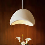 Clérachic Shibui pendant light seen close above the same dining table, its lit opening warming the calla lilies arranged just beneath.