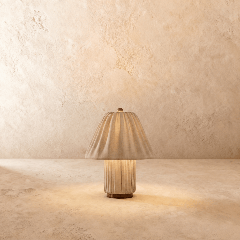 Clérachic table lamp in a pleated beige fabric shade over a matching fluted column base, glowing warm.