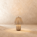 Clérachic table lamp in a pleated beige fabric shade over a matching fluted column base, glowing warm.
