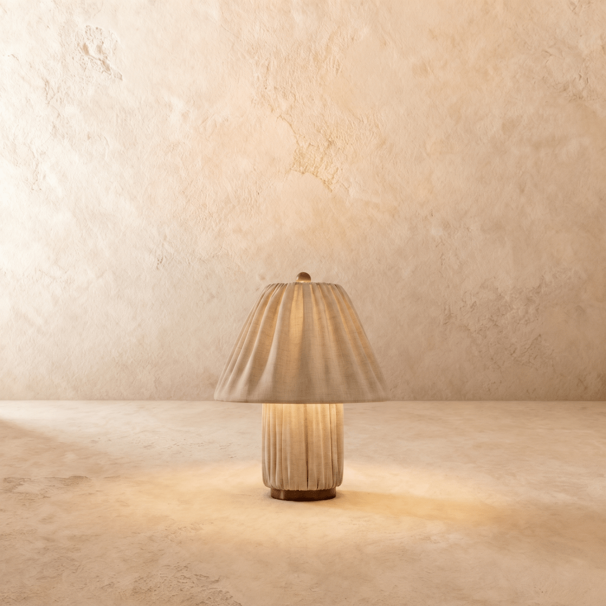 Clérachic table lamp in a pleated beige fabric shade over a matching fluted column base, glowing warm.
