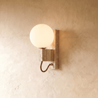 Clérachic wall lamp with a round opal glass globe on a travertine block, a brass arm curving below.