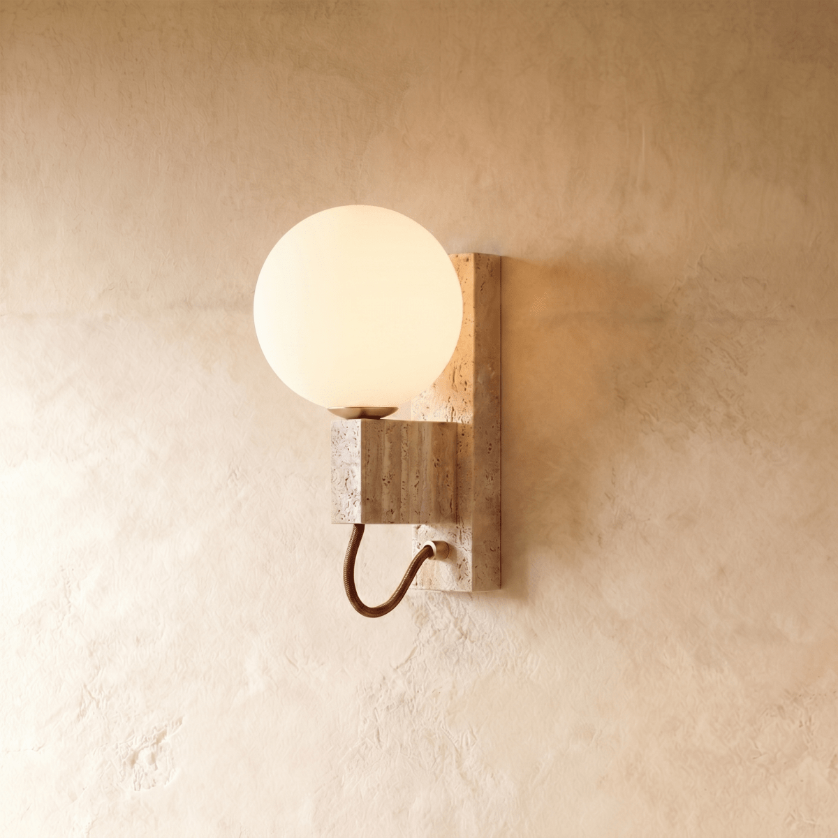 Clérachic wall lamp with a round opal glass globe on a travertine block, a brass arm curving below.